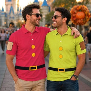 May include: Two polo shirts featuring a character-inspired design. One shirt is bright pink with two yellow circular buttons, a black belt graphic with a yellow buckle, and a tan elbow patch. The other is lime green with similar details.