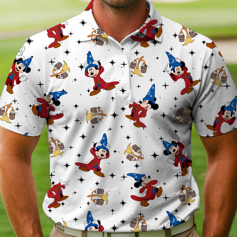 Puede incluir: Polo blanco con un patr&oacute;n repetido de Mickey Mouse con disfraz de mago, escobas y estrellas. La camisa tiene cuello y cierre de botones. El dise&ntilde;o incluye a Mickey con un sombrero de mago azul y una t&uacute;nica roja.
