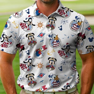 May include: White polo shirt featuring a nautical-themed pattern with Disney characters like Mickey Mouse, Donald Duck, and Goofy. The design includes anchors, ship wheels, and the Disney Cruise Line logo. The shirt has a classic collar and short sleeves.