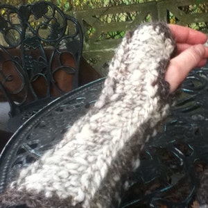 May include: A close-up of a white and gray knitted arm warmer. The arm warmer is made of a soft, fluffy yarn and has a textured pattern.