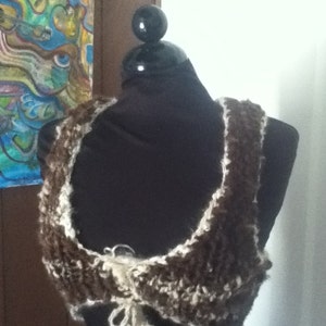 May include: A brown and white crocheted top with a tie at the front.