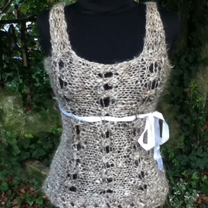 May include: A delicate, crocheted top with a lace pattern in a light brown color. The top features a white ribbon tied at the waist.