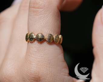 May include: Gold ring with a design of multiple seashells. The ring is worn on a person's finger.