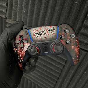 Puede incluir: Un mando de PlayStation 5 negro y rojo con el texto "RESIDENT EVIL 4" y una luz azul. El mando tiene detalles en rojo en los botones y joysticks, y un diseño salpicado.