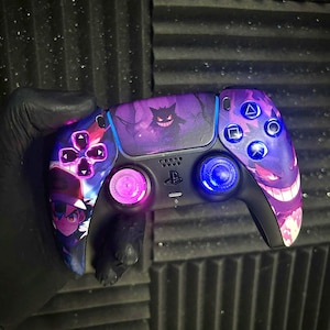 Könnte beinhalten: Benutzerdefinierter lila und blauer Videospiel-Controller mit einem Gengar-Design. Der Controller verfügt über beleuchtete Tasten und eine detaillierte Grafik der Pokémon-Figur. Das Design umfasst ein lila Steuerkreuz und pinke und blaue Joystick-Lichter.