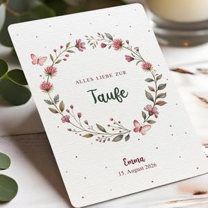Puede incluir: Una tarjeta blanca con un dise&ntilde;o de corona floral. La corona presenta flores rosas, hojas verdes y mariposas. La tarjeta tiene el texto "ALLES LIEBE ZUR Taufe" y el nombre "Emma" con la fecha "15. August 2026".