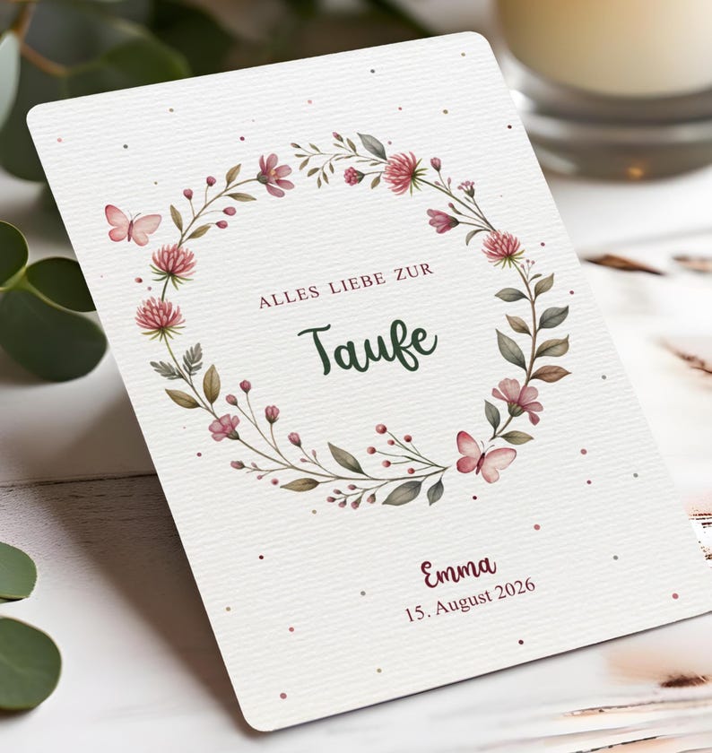Puede incluir: Una tarjeta blanca con un dise&ntilde;o de corona floral. La corona presenta flores rosas, hojas verdes y mariposas. La tarjeta tiene el texto "ALLES LIEBE ZUR Taufe" y el nombre "Emma" con la fecha "15. August 2026".