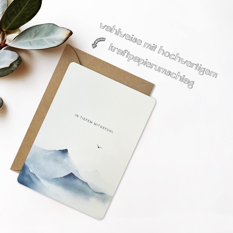 May include: A white greeting card with a watercolor mountain scene in shades of blue and gray, paired with a brown envelope. The card has the text "IN TIEFEM MITGEF&Uuml;HL" and a small bird illustration. The text "wahlweise mit hochwertigem kraftpapierumschlag" is also present.