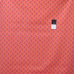 May include: A close-up of a pink fabric with a repeating pattern of small, diagonal lines in red, blue, and yellow. A ruler is included to show the scale of the pattern.