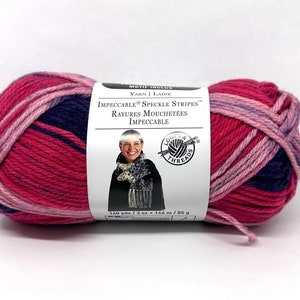 May include: A skein of Loops & Threads Impeccable Speckle Stripes yarn in a pink, purple, and navy colorway. The label reads "Impeccable Speckle Stripes" and "Rayures Mouchetées Impeccable". The yarn is 160 yards / 3 oz / 146 m / 85 g.