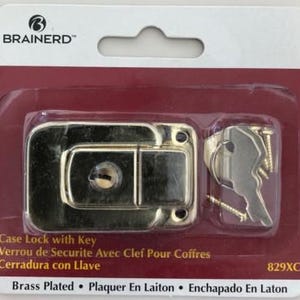 May include: A brass-plated case lock with a key, screws, and the Brainerd brand name. The lock is rectangular with rounded edges and a keyhole. The packaging includes text in English, French, and Spanish.