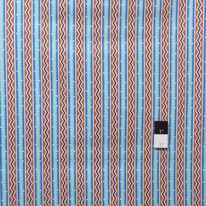 May include: A fabric with a repeating pattern of blue, orange, and white stripes. The stripes are made up of small zigzags and a line of small leaves. A ruler is included to show the scale of the fabric, which is 1 inch.