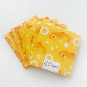 May include: A stack of eight yellow fabric squares with a white and orange seahorse pattern. The fabric is labeled "fabric quarters" and is 100% cotton.