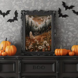 May include: A black framed print of a spooky forest scene with a ghost, flowers, and a crescent moon. The print is on a black shelf with a BOO sign and several orange pumpkins.