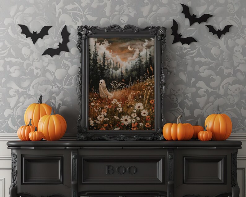 May include: A black framed print of a spooky forest scene with a ghost, flowers, and a crescent moon. The print is on a black shelf with a BOO sign and several orange pumpkins.