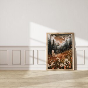 May include: A framed painting of a white ghost standing in a field of flowers. The background is a dark forest with a crescent moon in the sky. The painting has a vintage, ethereal feel.