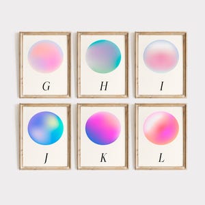 May include: Six framed art prints with a minimalist design. Each print features a gradient sphere in shades of pink, blue, and purple. The letters G, H, I, J, K, and L are printed below each sphere. The frames are a light brown colour.