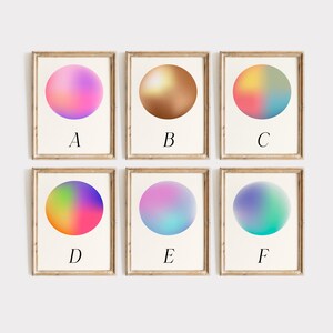 May include: Six framed art prints with colourful, gradient orb designs. Each print features a different colour scheme, including pink, gold, and blue. The letters A through F are printed below each orb. The frames are a light brown colour.