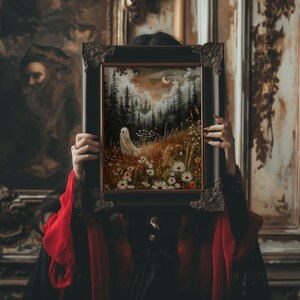 May include: A woman in a red and black dress holds a framed painting in front of her face. The painting depicts a forest scene with a white ghost figure in the foreground and a crescent moon in the sky.