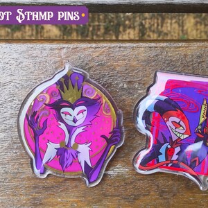 Peut inclure: Deux &eacute;pingles en acrylique transparent repr&eacute;sentant des personnages de la s&eacute;rie anim&eacute;e "Helluva Boss". La premi&egrave;re &eacute;pingle repr&eacute;sente un personnage violet et rose avec une couronne et un sourire malicieux. La deuxi&egrave;me &eacute;pingle repr&eacute;sente un personnage rouge et noir avec un sourire diabolique tenant un pistolet.
