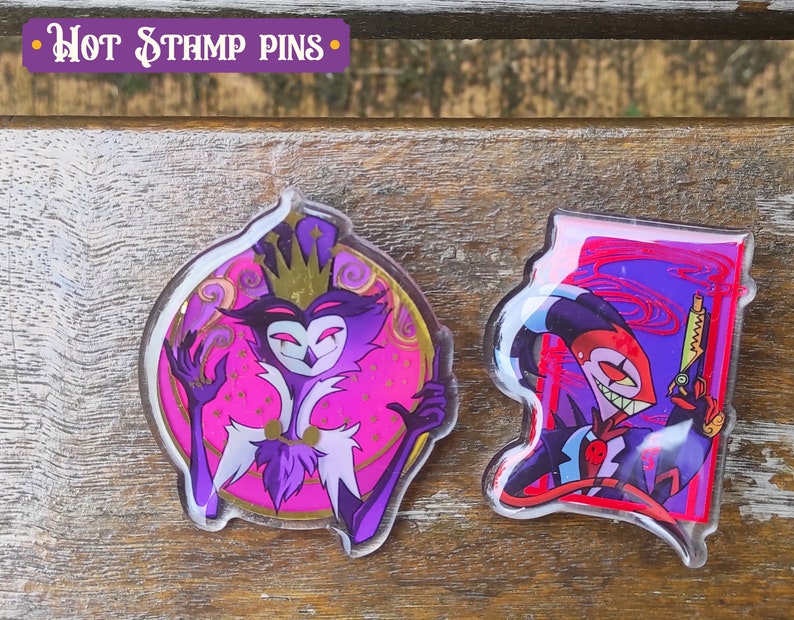 Peut inclure: Deux &eacute;pingles en acrylique transparent repr&eacute;sentant des personnages de la s&eacute;rie anim&eacute;e "Helluva Boss". La premi&egrave;re &eacute;pingle repr&eacute;sente un personnage violet et rose avec une couronne et un sourire malicieux. La deuxi&egrave;me &eacute;pingle repr&eacute;sente un personnage rouge et noir avec un sourire diabolique tenant un pistolet.