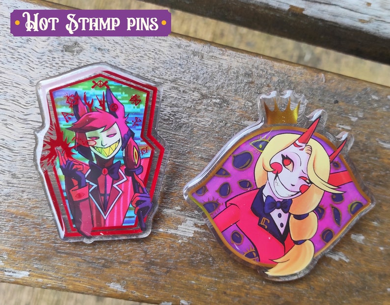 Peut inclure: Deux &eacute;pingles en acrylique repr&eacute;sentant des personnages de la s&eacute;rie anim&eacute;e "Hazbin Hotel". La premi&egrave;re &eacute;pingle est une &eacute;pingle en forme de cercueil rouge et noir avec une image de dessin anim&eacute; d'un d&eacute;mon aux cheveux roux avec des cornes et un n&oelig;ud papillon. La deuxi&egrave;me &eacute;pingle est une &eacute;pingle ronde avec une image de dessin anim&eacute; d'un d&eacute;mon blond avec des cornes et un n&oelig;ud papillon. L'arri&egrave;re-plan de la deuxi&egrave;me &eacute;pingle est violet avec des yeux dor&eacute;s.
