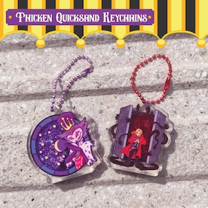 May include: Two acrylic keychains with character designs. One features a purple and white character in a stained-glass style circle, the other a character in a red coat. Both have chain attachments. The text "Thicken Quicksand Keychains" is at the top.