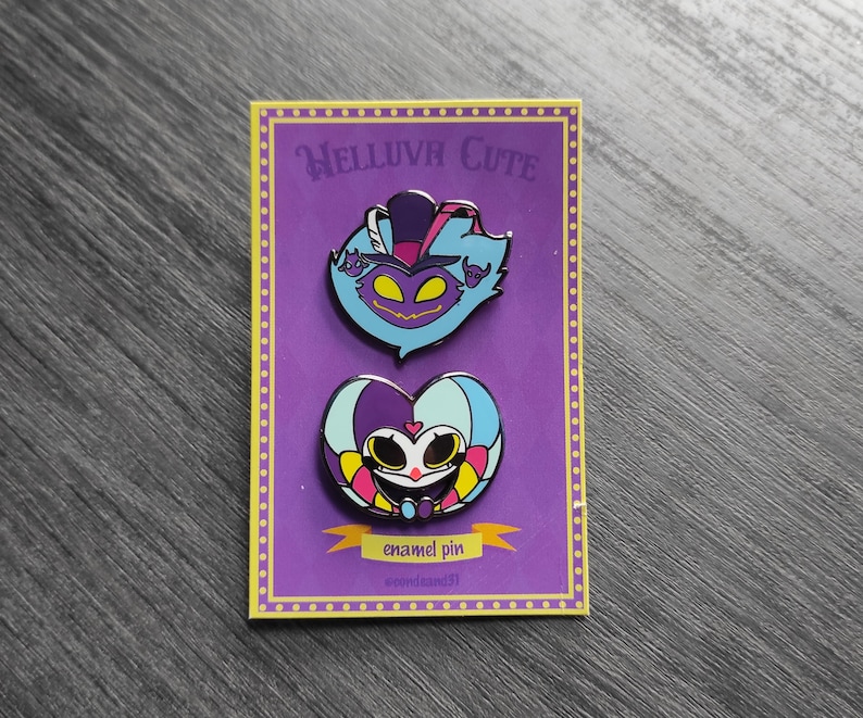 Peut inclure: Deux &eacute;pingles en &eacute;mail sur une carte violette. L'&eacute;pingle sup&eacute;rieure est un personnage de dessin anim&eacute; bleu et violet avec un chapeau. L'&eacute;pingle inf&eacute;rieure est un personnage en forme de c&oelig;ur avec un visage. La carte indique "HELLUVA CUTE" et "&eacute;pingle en &eacute;mail".