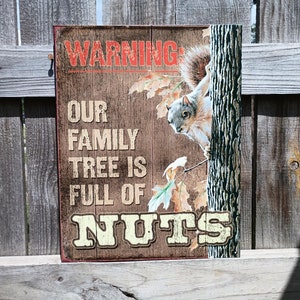 May include: A rustic brown metal sign with the text "WARNING: OUR FAMILY TREE IS FULL OF NUTS" and a cartoon squirrel peeking out from behind a tree trunk.
