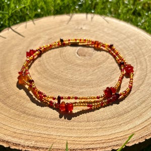 May include: A double-strand beaded bracelet. The bracelet is made with small, golden beads and red and orange accents. The bracelet is displayed on a wooden surface.