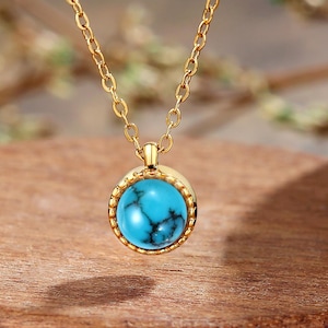 May include: A gold chain necklace with a turquoise stone pendant. The pendant is round and has a gold border.