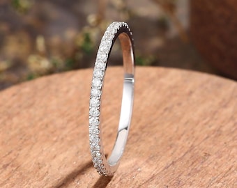May include: A thin, silver-toned metal band ring featuring a continuous row of small, clear, round-cut stones set along the outer surface. The ring has a polished, reflective finish and a slender profile, showcasing a classic, delicate design.