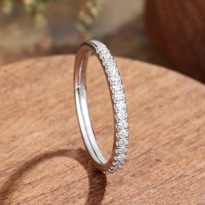 May include: A thin silver band ring with a row of small, clear diamonds encircling the band.