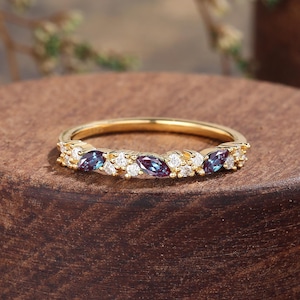 May include: A gold band ring with a row of marquise-shaped gemstones. The ring features alternating clear and purple-blue stones.