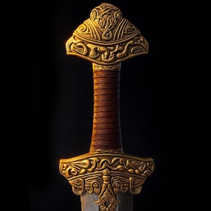 May include: A close-up of a sword hilt and part of the blade. The hilt is gold-colored with intricate carvings and a brown leather-wrapped grip. The blade is a silver-gray color. The background is black.