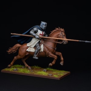 Puede incluir: Miniatura detallada de un caballero con armadura completa montado a caballo marrón, con una lanza. El caballero lleva una túnica blanca con una cruz roja, una capa azul y un casco. El caballo está sobre una base con hierba.