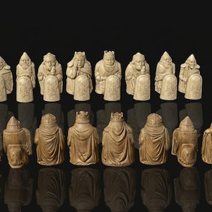 May include: A complete chess set featuring intricately carved ivory-colored pieces. The set includes kings, queens, bishops, knights, rooks, and pawns, each with unique details. The pieces are arranged on a reflective black surface.