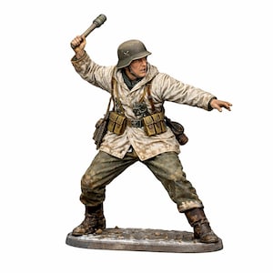 May include: A detailed figurine of a soldier in a winter camouflage uniform, poised to throw a grenade. The figure wears a helmet, carries pouches, and is set on a small, textured base. The color palette includes shades of white, brown, and green.