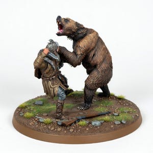 Puede incluir: Escultura en miniatura detallada que representa a un hombre luchando contra un oso pardo. El oso ruge con la boca abierta, y el hombre sostiene un cuchillo. Un rifle yace en el suelo cerca de la base circular marrón con hierba y rocas.