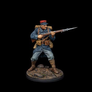 May include: A miniature figurine of a soldier in a blue uniform, red cap, and brown boots, holding a rifle with a bayonet. The figure has a mustache and is standing on a circular base. The background is black.
