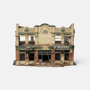 Könnte beinhalten: Ein detailliertes Modell eines zweistöckigen, verfallenen Gebäudes. Die Fassade ist beige mit grünen und roten Akzenten, mit zerbrochenen Fenstern und beschädigten Wänden. Das Modell vermittelt einen Eindruck von Verlassenheit und Verfall.