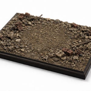 Puede incluir: Base de diorama rectangular con marco de madera oscura. La superficie está cubierta de pequeñas rocas, tierra y escombros, con ladrillos y vigas de madera en miniatura dispersos. La paleta de colores es de tonos tierra.