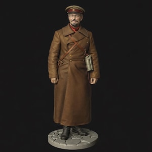 May include: A detailed miniature figure of a man in a brown overcoat, cap, and glasses. The figure has a red scarf and a leather strap across the chest. A small bag hangs from the strap. The figure stands on a stone-like base.