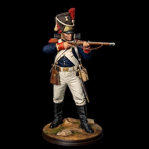 May include: A detailed figurine of a soldier in a blue coat, white trousers, and black boots, holding a rifle. The soldier wears a tall black hat with a red plume. The figure stands on a small, round base with a detailed, realistic appearance.
