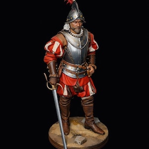 May include: A detailed figurine of a soldier in historical attire. The figure wears a silver helmet with a plume, a metal breastplate, and a red and white doublet. He holds a sword, standing on a circular base with a sandy texture. The overall aesthetic is realistic.