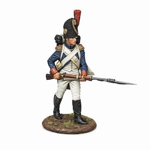 May include: A miniature figurine of a soldier in a blue coat, white pants, and black boots, holding a rifle with a bayonet. The soldier wears a black hat with a red plume and stands on a small, round, earthy base. The figure is a historical representation.