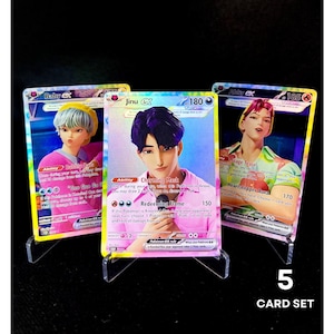 May include: Three Pokémon EX trading cards on clear stands. The cards feature illustrations of anime-style characters with various abilities and attack powers. The text "5 CARD SET" is visible at the bottom.