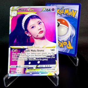 May include: A collectible Pokémon VSTAR card featuring a woman with a white headband. The card has a pink and purple background with the text "Moka VSTAR" and "Caffè Moka Aroma". The card is displayed with another Pokémon card.
