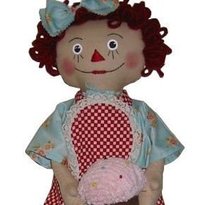 May include: A handmade rag doll with red curly hair, a blue and white dress, and a pink and brown cupcake.