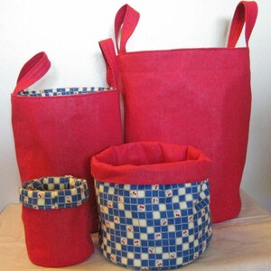May include: Three red fabric storage bins with handles. The largest bin is plain red, while the two smaller bins have a blue and white checkered pattern with red accents.